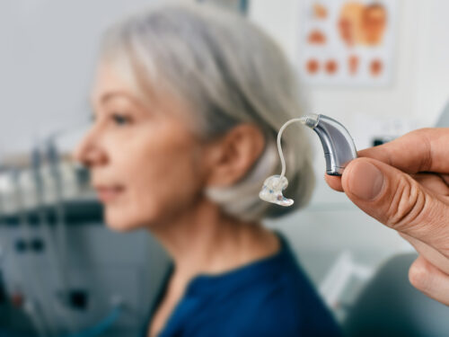 Close-up of hearing aid near senior patient's ear at audiology clinic