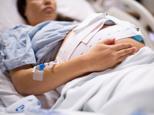 A pregnant woman in the hospital with an IV drip and a cardiograph.